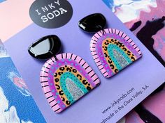 two pairs of earrings are on top of a purple and blue card with the words i love my soda