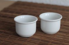 two white cups sitting on top of a bamboo mat