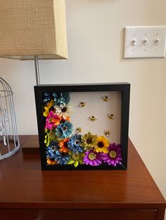 a shadow box with flowers in it sitting on a table next to a lamp and a birdcage