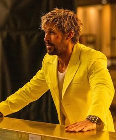 a man in a yellow suit leaning on a counter with his hand on the table