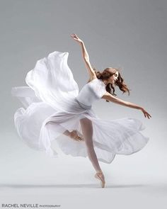 a woman in a white dress is dancing with her arms spread out and legs extended