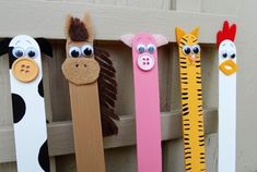 four different colored toothbrushes with animal faces on them, lined up against a wooden fence