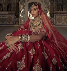 a woman in a red bridal gown sitting on the floor with her arms crossed