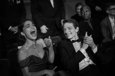 black and white photograph of two women laughing in front of other people at an event