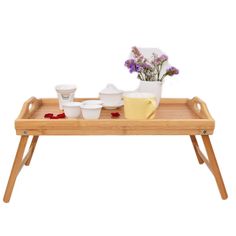 a wooden tray with flowers and bowls on it, sitting on a table next to a cup