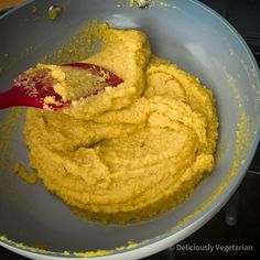 a bowl filled with yellow food and a red spatula in the bottom right hand corner