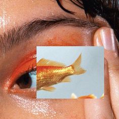 a person holding up a card with a goldfish on it's side to their eye