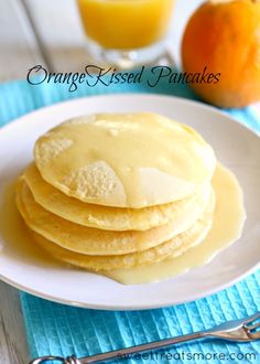 a white plate topped with pancakes on top of a blue table cloth next to a glass of orange juice