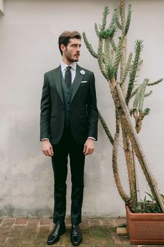 a man in a suit and tie standing next to a cactus tree with his hands in his pockets