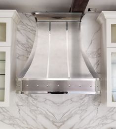 a stainless steel range hood mounted on the side of a white kitchen wall with glass cabinets