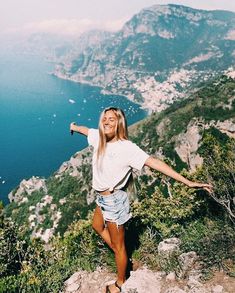 a woman standing on the edge of a cliff with her arms spread out and smiling