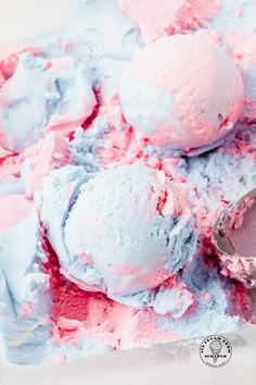 two scoops of pink and blue ice cream are in a bowl with spoons