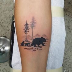 a black bear and cubs tattoo on the left arm, with trees in the background