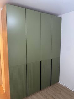 an empty room with green cupboards and wood flooring on the walls, in front of a white wall