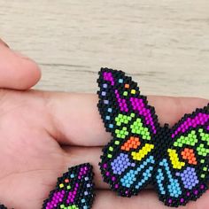 a hand holding a small beaded butterfly on it's thumb and another one in the background