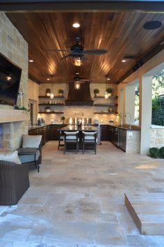 an outdoor kitchen and dining area with stone flooring, built - in fireplaces and ceiling fans