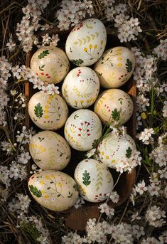 an arrangement of painted eggs in a basket on the ground with flowers and branches around them