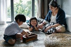 two children and an adult sitting on the floor playing with wooden blocks in front of a window