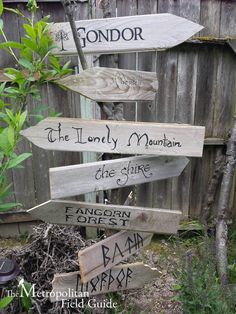 several wooden signs pointing in different directions on a fenced in area with trees and flowers