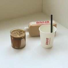 there are two cups and a container on the table next to each other, one has a straw in it