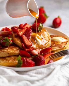 pancakes with strawberries and syrup being poured onto them