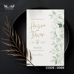 a wedding card with white flowers and greenery on the front, next to a black plate