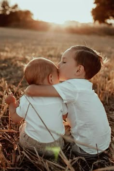 two children are sitting in the grass and kissing each other's foreheads as the sun sets behind them