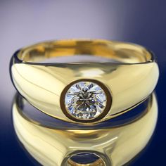 a yellow gold ring with a round brilliant diamond in the center on a reflective surface