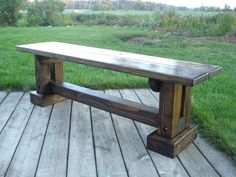 a bench sitting on top of a wooden deck next to a lush green grass covered field