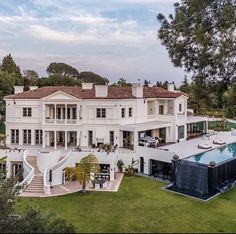 an aerial view of a large white house with a pool in the foreground and trees surrounding it