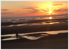 the sun is setting at the beach with people walking on it