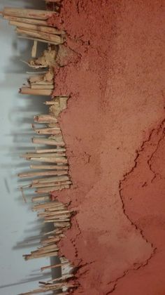 a pile of sticks sitting on top of a red dirt covered ground next to a white wall