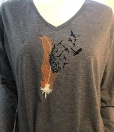 a woman's gray shirt with an orange feather on the front and black birds on the back