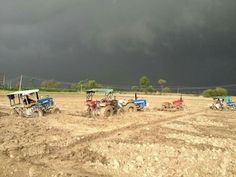 four tractors are parked in the dirt under a dark sky with storm clouds behind them