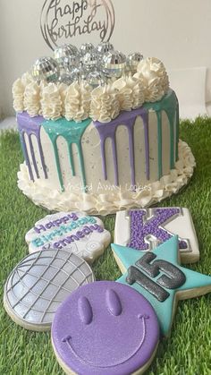 decorated cookies sitting in the grass next to a birthday cake and cookie cutters on top of it