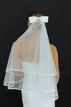 a woman wearing a white veil with a bow on it's head is looking down at her wedding dress