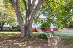 a wooden bench sitting under a tree in front of a house