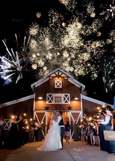 a bride and groom standing in front of a barn with fireworks