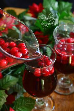 cranberry sauce being poured into two glasses filled with red berries and greenery