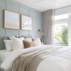 a bedroom with blue walls, white bedding and two framed pictures on the wall