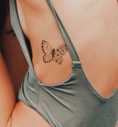 a woman with a butterfly tattoo on her upper arm and lower back side, sitting in a green tank top