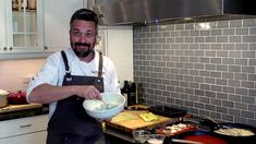 a man standing in a kitchen holding a bowl with food on the counter and cooking utensils