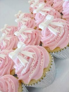 cupcakes with pink frosting and white bows on them are arranged in rows