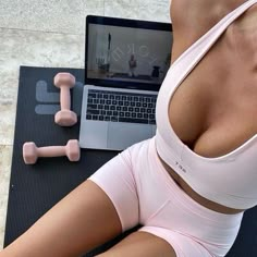 a woman laying on top of a yoga mat next to a laptop and dumbbells