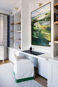 a painting hangs on the wall above a desk in a room with built - in bookshelves