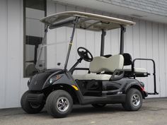 a green golf cart parked in front of a white building with the door open and seat up