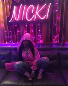 a woman sitting on top of a black couch in front of a neon nicki sign