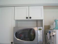 a silver microwave oven sitting on top of a white cabinet above a refrigerator freezer