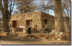 an old stone house in the woods with trees and rocks on the ground around it