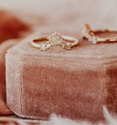 two gold rings sitting on top of a pink velvet cushioned box with white feathers